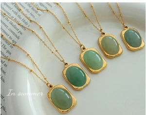 Detailed view of five vintage 18K gold plated square pendants with green gemstones on a white plate
