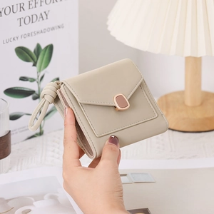 Close-up of beige trifold wallet featuring metallic buckle and braided knot charm detail