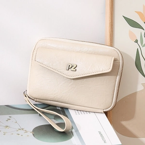 Détail d'une pochette en cuir beige avec logo PZ doré, dragonne et fermeture éclair