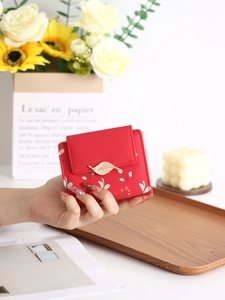 Gros plan d'un petit portefeuille rouge à fleurs avec boucle en feuille dorée