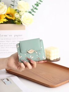 Détail du portefeuille vert menthe avec fermoir feuille dorée et motif floral en main
