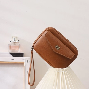 Détail d'une pochette en cuir grainé marron avec logo PZ et dragonne élégante