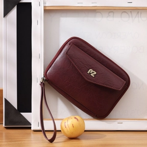 Détail de la texture cuir bordeaux avec dragonne et logo PZ en métal doré sur le sac