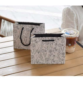 Detail view of floral line art gift bags with black woven handles on a wooden table