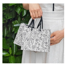 Detail of white gift bags with black floral line art and sturdy black woven handles