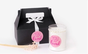 Detail of black gift box with pink YOU are loved sticker and scented glass candle