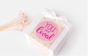 Square white gift box with white satin ribbon and pink 'YOU are loved' textured sleeve