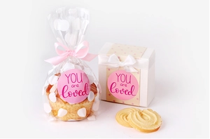 Close-up of pink round stickers with YOU ARE LOVED text on gift boxes and bags