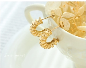 Detail of gold C-shaped hoop earrings with spiral texture on a ceramic cup edge