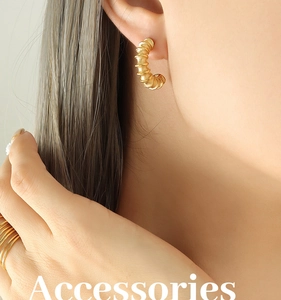 Macro detail of gold C-shaped spiral earrings and multi-layer rings on a model