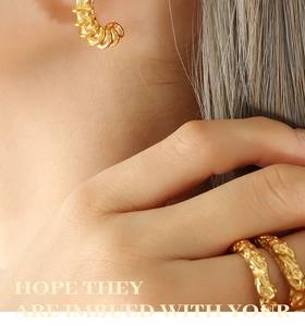 Close-up of elegant gold-plated threaded C-shaped earrings and textured rings on model
