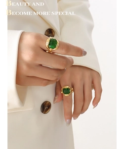Detail of cross-over gold ring with emerald-cut green crystal worn on hand