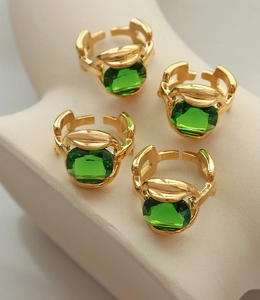 Detail of adjustable gold rings featuring emerald green crystals and chain link design