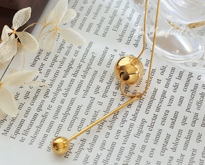Detail of a gold-plated snake chain necklace with spherical and bar tassels on a vintage background