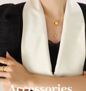 Detail of minimalist gold-plated necklace and rings worn with elegant tweed jacket