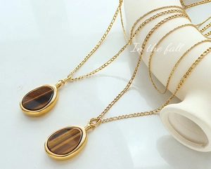 Macro shot of tiger eye stone pendants and gold Figaro chains on a ceramic bowl