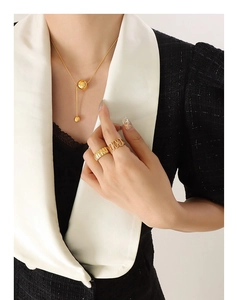 Close-up of golden ball tassel Y-necklace and textured rings on a model in chic attire