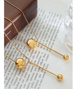 Detail shot of golden snake chain necklace with spherical bead and long tassel pendant