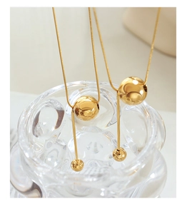 Detailed close-up of a gold snake chain necklace with a minimalist bead and bar tassel pendant