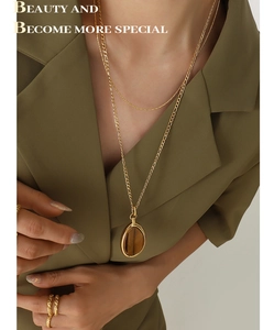 Detail of layered gold titanium necklace featuring an oval tiger eye stone pendant