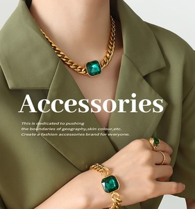 Chunky gold-plated chain set with emerald green crystals on a model in olive blazer