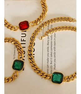 Close-up of gold Cuban chain with large rectangular emerald and ruby crystal pendants