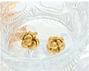 Macro detail of 18K gold-plated chunky flower stud earrings in a crystal glass bowl