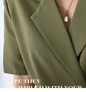 Detail of gold chain necklace with iridescent shell pendant on olive green blazer