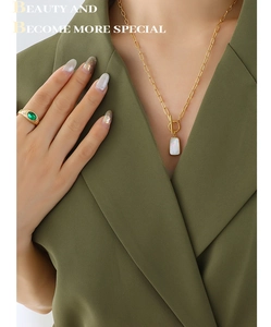 Detail of gold chain necklace with shell pendant and emerald green gemstone ring on model