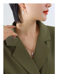 Detail of elegant gold necklace and shell earrings on a model in an olive suit