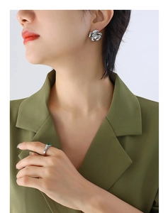 Close-up of model wearing silver rose earrings and a green gemstone ring