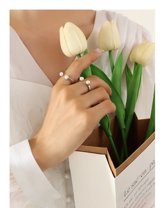 Detail of silver U-shaped open rings with natural pearls held against yellow tulips