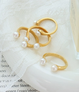 Detail view of four baroque pearl gold rings with U-shape open design on lace background