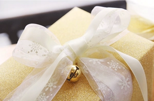 Close-up of white snowflake ribbon and golden bell on a sparkling gift box
