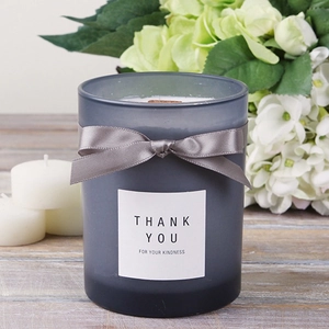 Grey frosted glass scented candle with wood wick and ribbon bow on vintage wood background