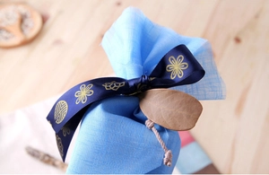 Close-up of sky blue gift pouch with gold-stamped dark blue ribbon and dried leaf tag
