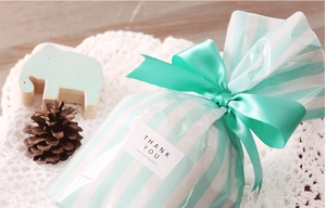 Detalle de bolsa de regalo a rayas azul claro con cinta de raso y pegatina de gracias