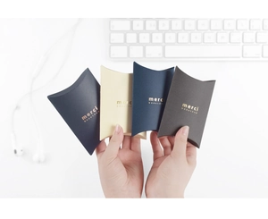 Close-up of small pillow-shaped gift boxes in four colors with gold foil merci lettering