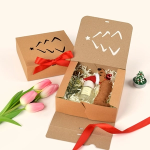 Kraft paper gift box with Christmas tree cutout and red bow featuring plush dog and candle