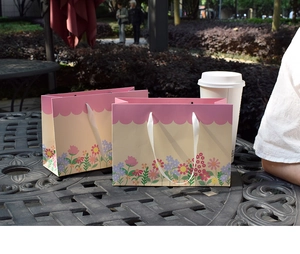 Close-up of floral gift bags with pink wavy edges and white silk ribbon handles outdoors