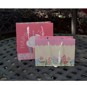 Detail of floral paper gift bags with white ribbon handles and festive cake patterns