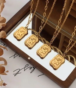 Macro view of gold plated square butterfly relief pendants on a warm wood mirror surface