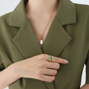 Minimalist gold necklace with shell pendant and green stone ring set on olive suit model