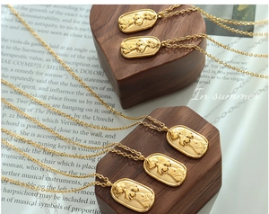 Detailed close-up of gold oval pendant with abstract female body relief on wood surface
