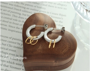 Detail of C-shaped silver and gold interlocking hoop earrings on wooden heart base