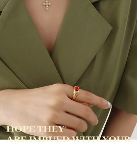Détail d'un collier croix doré avec perles et bague rubis porté par un mannequin