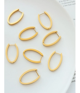 Détail de boucles d'oreilles créoles ovales dorées en acier titane sur plateau céramique
