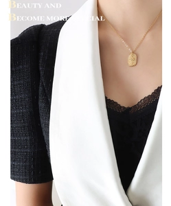 Detail of gold oval relief pendant necklace worn with a stylish black tweed jacket