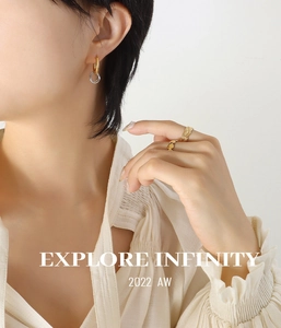 Close-up of interlocking metal earrings and gold rings worn with a white blouse