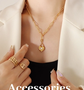 Gros plan sur le collier cadenas cœur doré et bagues gourmettes avec blazer ivoire